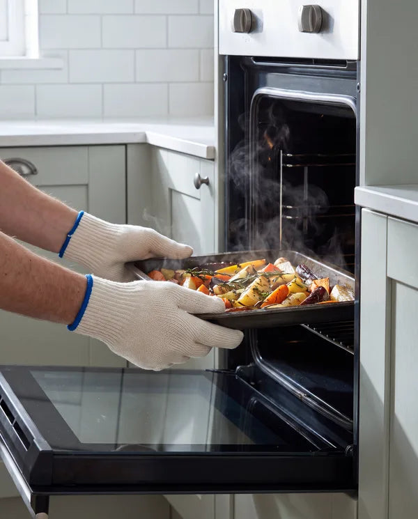 Hands in V TOWER knit heat-resistant gloves lifting a tray from the oven